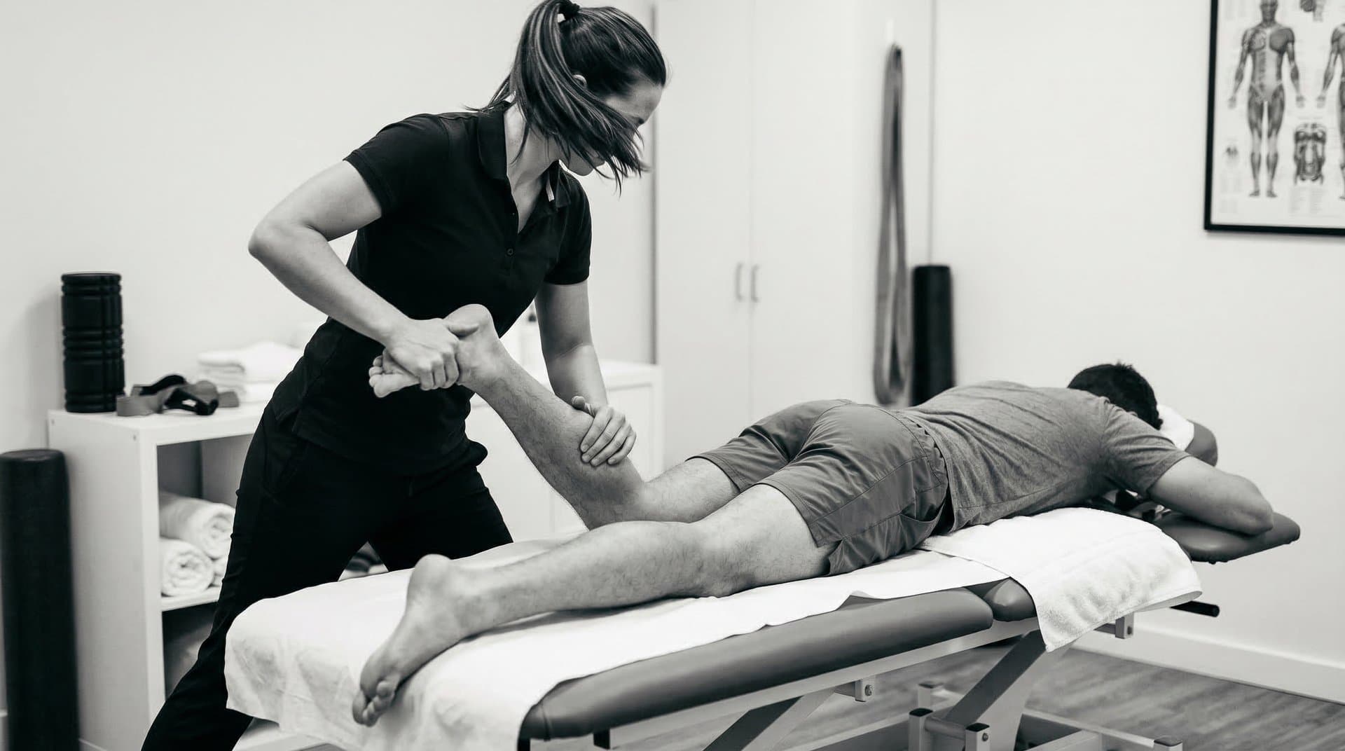 Therapist assisting a client with a leg stretch on the massage table, demonstrating dynamic sports massage technique