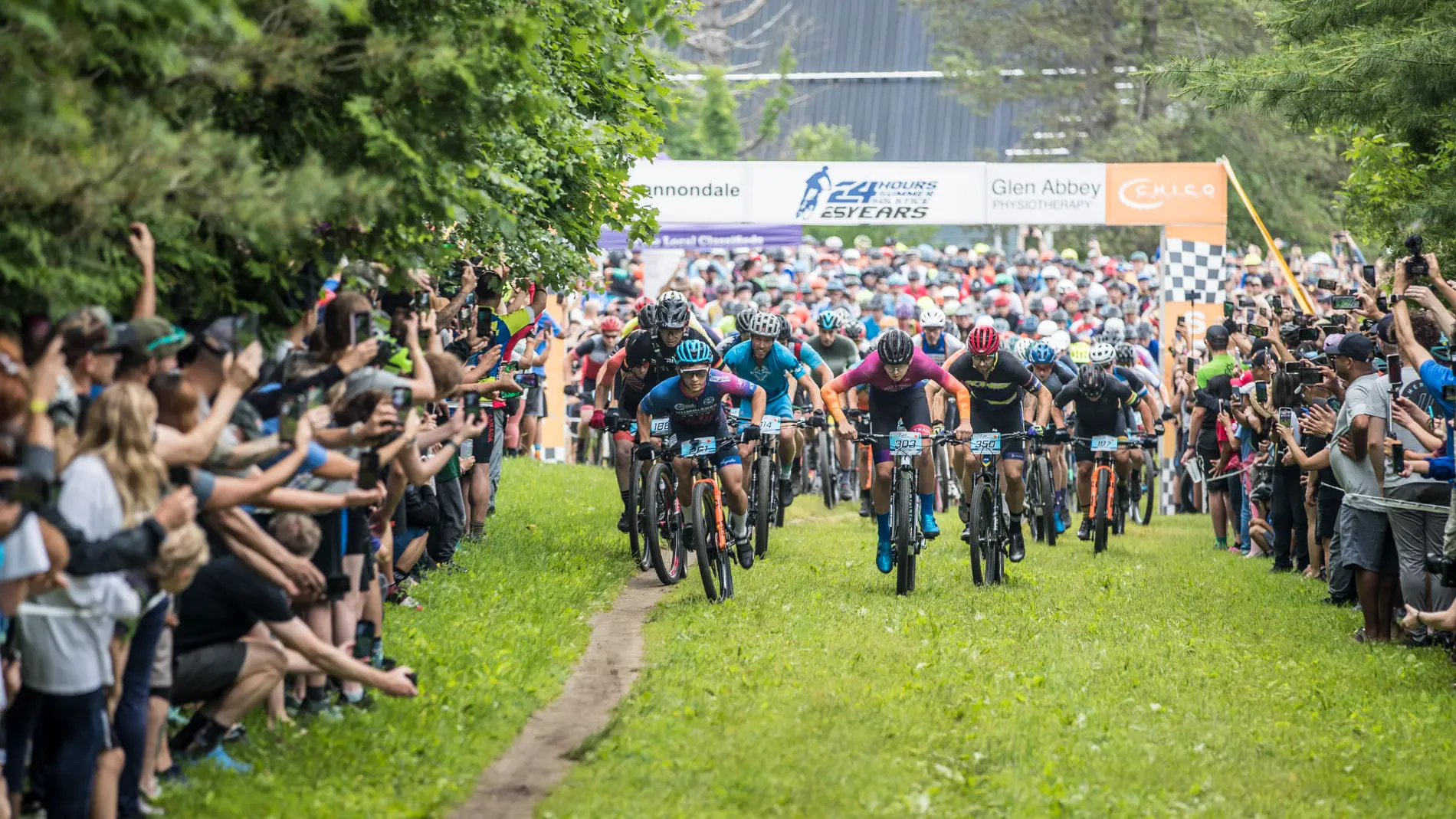 Riders at the mass start of the 24 Hours Summer Solstice mountain bike race, lined by cheering spectators